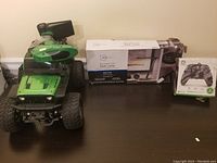 Green remote control off-road vehicle, boxed desk lamp, and boxed Xbox controller placed on a dark surface and photographed from above at an angle.