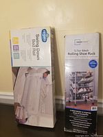 Both boxed items shown standing next to each other against wall: Regalo Swing Down Bed Rail box and Mainstays 5-Tier Mesh Rolling Shoe Rack box