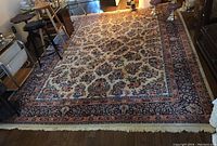 Full view of the large rectangular oriental rug laid out on a wooden floor inside a room with miscellaneous furniture around it.