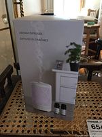Box of aroma diffuser and two bottles of essential oils shown on sitting surface.