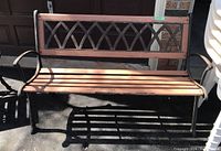 Front view of outdoor bench showing wooden seat slats and decorative cast iron backrest.