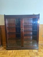 Front view of the book cabinet showing two glass doors and wooden shelves inside, reflecting light from the room.
