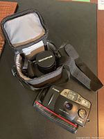Canon SureShot OWL camera with Olympus camera in its carrying case, placed on black surface.