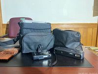 Two cameras and two black carrying bags on a table. Kodak Star 110 film camera and Canon Rebel EOS K2 3000V with attached lens are visible along with camera bags.