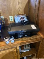 Canon PIXMA MG2500 printer with two extra ink cartridges on the left side, placed on a wooden surface.