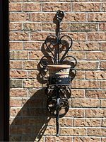 Full frontal image of cast iron wall sconce holding clay pot against brick wall
