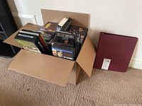 Cardboard box filled with over 50 CDs and DVDs, viewed from overhead showing the collection packed inside.