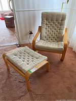 Front view of the Ikea chair and matching ottoman set on carpet in room, showing beige cushions and wood frame.