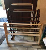 Wooden quilt stand and two towel racks positioned behind a white folding clothes drying rack. All items show signs of scratches and scuffs.
