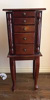 Front view of wood jewelry stand showing five drawers, two carved wood columns on sides, and cabriole legs, with polished finish.