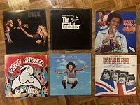 Photo showing six LP album covers including Fleetwood Mac's Mirage, The Godfather soundtrack, Bobby Vinton's Greatest Hits, Bette Midler's No Frills, Leo Sayer album, and The Beatles' Story album.