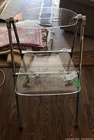 Front and side angled view of a clear acrylic chair with chrome frame showing seat, backrest and frame details.