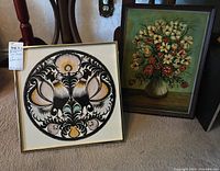 Two framed artworks side by side: bird-themed circular cut paper art and floral still life painting on board.