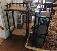 Photo showing two plant stands: a rectangular caned wood plant stand with two shelves and a round three-tier wood stand