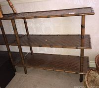 Front and angled view showing three shelves made of woven rattan supported by cylindrical rattan poles resembling bamboo.