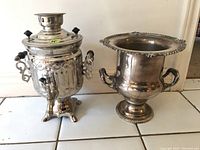 Full view of the electric samovar alongside the silver-plated champagne bucket on a tiled surface against a white wall.