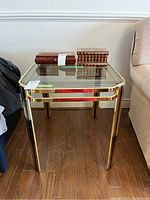 Front view of brass finish steel side table with clear glass top showing rectangular shape and leg structure on wooden floor.