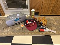 Photo showing all the items laid out including the Sony radio, tennis rackets, balls, baseball glove, boxing gloves, red baseball cap, and playing cards.