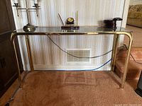 Full front view of the metal base table with clear glass top, showing polished golden metal legs and frame with some decorative objects on top.