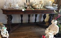 Front side view of vintage ornate wood table with carved legs and decorated stretcher base. Contents on table surface include various glassware and porcelain items but are not part of the lot.