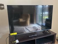 Front view of Skyworth 50 inch TV with remote placed on TV stand, showing reflective black screen and V-shaped legs.