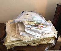 Stack of various vintage linens and doilies folded on a wooden table including some crocheted pieces.