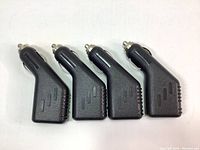 Four identical black USB car lighter chargers aligned side by side showing the metallic contact tips.