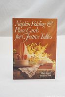 Front cover of the hardcover book showing the title and an artfully folded napkin on a table with flowers.