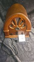 Front view of wooden cathedral-style radio showing carved decorative grill, frequency window, knobs and electric cord