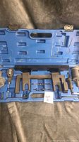 Blue plastic case opened displaying metal components of camshaft tool set, case shows scuffs and damage, tools arranged inside.