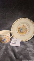 Photo of Bunnykins cup and plate showing overall design and condition, placed on grey cloth background.