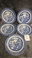 Five blue and white Willow pattern Churchill plates including four oval and one round plate, shown on dark surface.