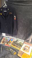 Military jacket hanging on a hanger next to four collector magazines and a boxed collectible set with 14 small plastic military figurines arranged in front.