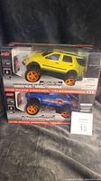 Photo of two brand new, unopened RevZone 1:20 scale radio controlled trucks, yellow SUV and blue off-road truck, still in packaging.