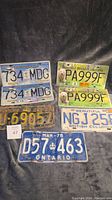 Top view of multiple license plates, including BC Olympic, BC Parks, and vintage plates from Ontario
