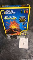 Front and side views of unopened National Geographic volcano kit box with visible branding and warnings.