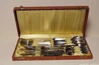 Closed view of the silver plate flatware in an open lined brown case showing a portion of the contents spread out.