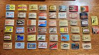 Top down view of all 50 vintage foreign made matchbox labels arranged in rows on a wood table.