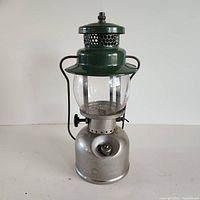 Front view of nickel plated Coleman lantern showing green top and clear glass globe with metal frame and handle