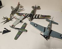 Group of seven vintage die cast model airplanes from various military forces and eras displayed on a flat surface, showing varying paint schemes and insignias.