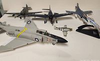 Top and angled view of various vintage die cast model airplanes on a surface showing six models including Navy jet and other military planes.