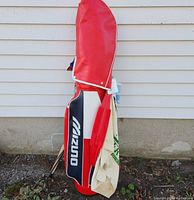 Photo showing front side of red, white, and black Mizuno golf bag standing upright with towel and some golf club shafts visible