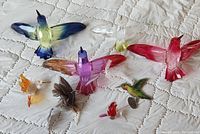 All eight hummingbird sun catcher ornaments arranged on a quilted white fabric surface showing variety in colors and sizes.