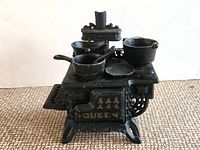 Front angle showing the Queen branded miniature cast iron stove with pots and pans on the stove top.