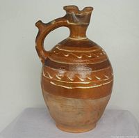 Front view of red clay jug with hand-painted cream bands and patterns on reddish-brown body, showing rounded body, handle and uniquely shaped spout.