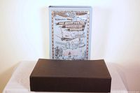 Photo showing the book with the slipcase on a white surface, slipcase is dark brown.