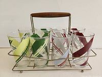 View of eight vintage drinking glasses with angled colored stripes (yellow, green, white, red) in a metal carrier with wooden handle