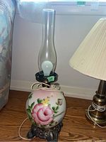 Full view of the antique lamp showing the floral painted glass globe in pink and green, clear glass chimney, and ornate resin base.