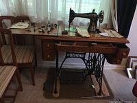 Full view of sewing machine installed in wooden cabinet with cast iron base and attachments laid out on top