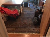 The full room view showing the area rug laid on hardwood floor beneath furniture, with bags and other items around it, demonstrating size and condition.